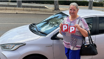 Yvonne standing in front of her car, holding her P Plates.